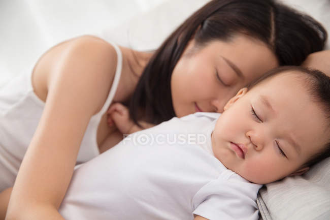 Nahaufnahme der schönen jungen asiatischen Mutter und des entzückenden Säuglings, der zusammen auf dem Bett schläft — Stockfoto
