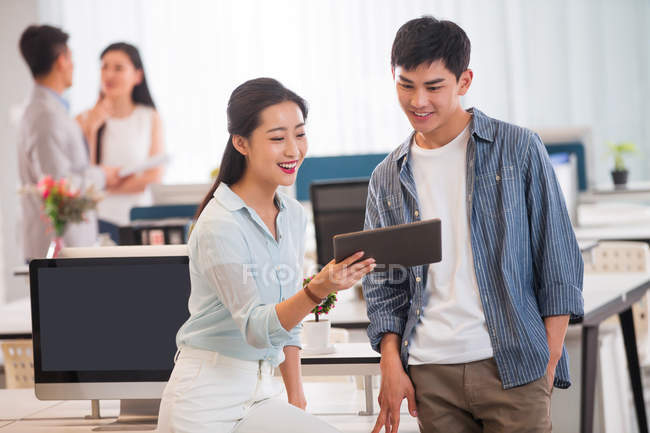 Sorridente giovane uomo d'affari asiatico e donna d'affari utilizzando tablet digitale e discutendo del progetto in ufficio — Foto stock