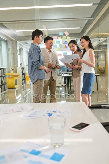Усміхнені молоді азіатські бізнесмени і бізнесмени стоять разом і обговорюють документи в офісі — стокове фото