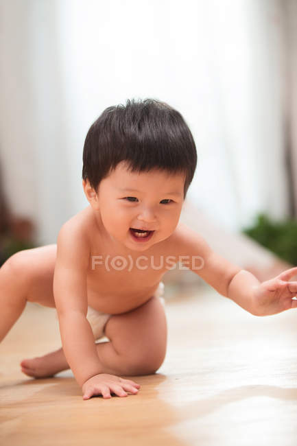Beau bébé asiatique heureux en couche rampant sur le sol et riant à la maison — Photo de stock