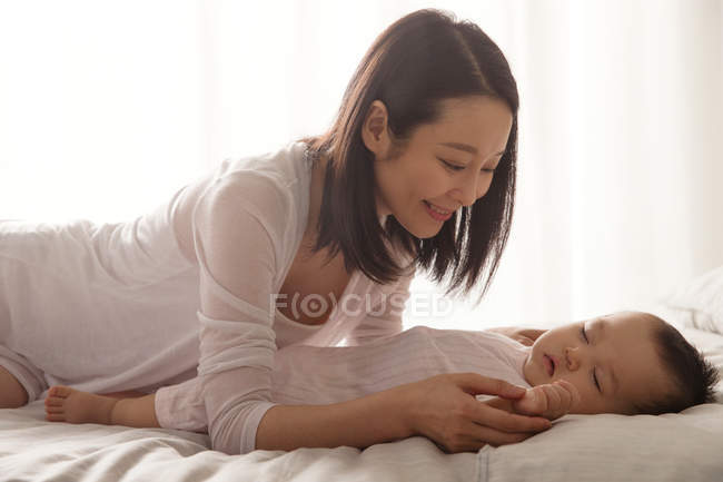 Felice giovane donna asiatica guardando bello bambino dormire sul letto — Foto stock