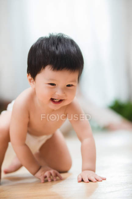 Чарівний щасливий азіатський малюк в підгузник повзе на підлозі вдома — стокове фото