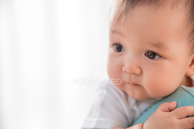 Cropped shot of parent carrying adorable asian infant child looking away at home — Stock Photo
