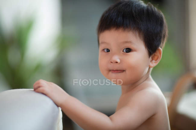 Боковой вид восхитительного ребенка, прислонившегося к дивану и смотрящего в камеру — стоковое фото