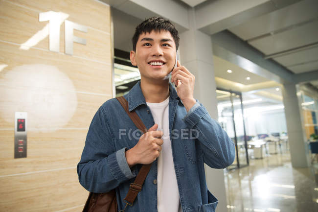 Guapo feliz joven empresario hablando por teléfono inteligente en la oficina - foto de stock