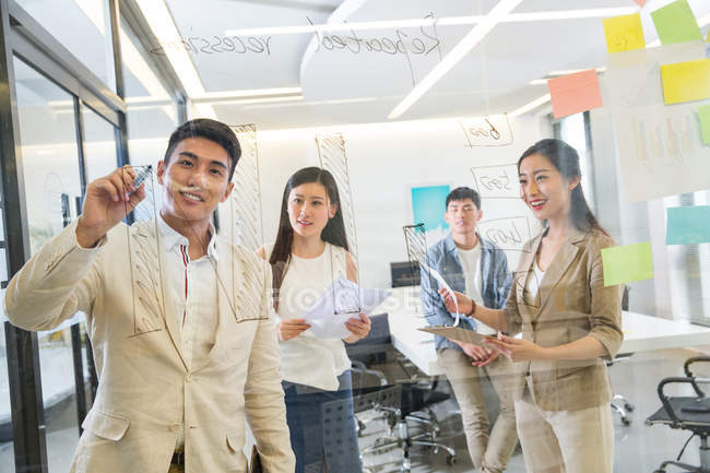 Просмотр через стекло молодых азиатских бизнесменов, делающих заметки во время встречи в офисе — стоковое фото