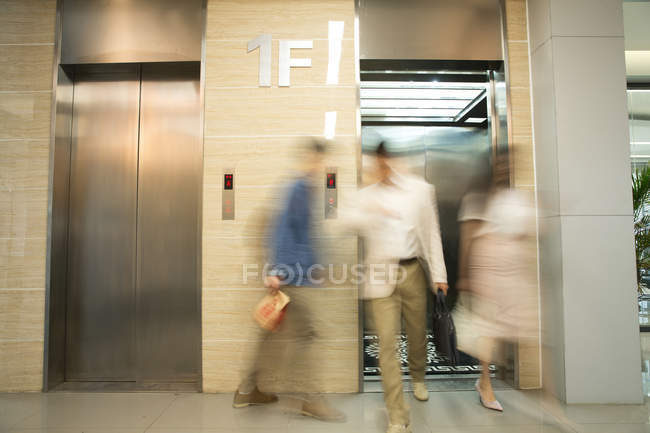 Giovani uomini d'affari sfocati a piedi vicino ascensore in ufficio moderno — Foto stock