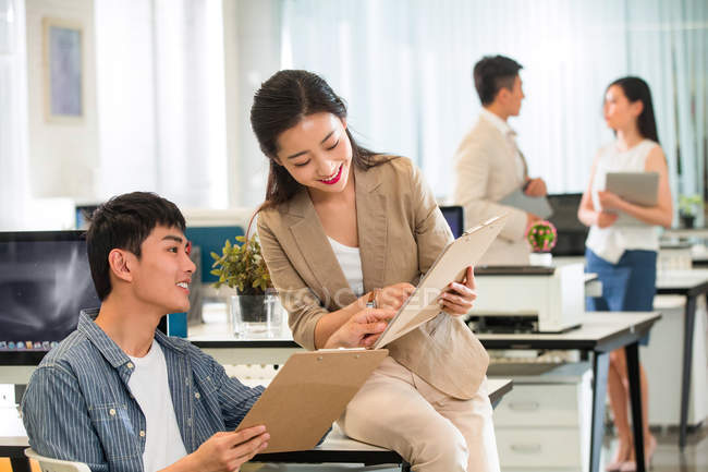 Smiling young asian businessman and businesswoman discussing work in modern office — Stock Photo