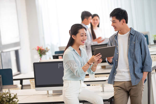 Счастливый молодой бизнесмен и деловая женщина с помощью цифрового планшета и обсуждения работы в офисе — стоковое фото