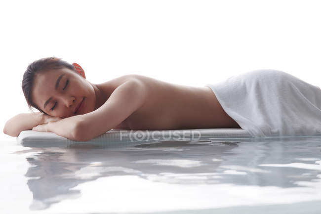 Вид збоку красива усміхнена азіатська жінка з закритими очима лежить з рушником на тілі в спа-салоні — стокове фото