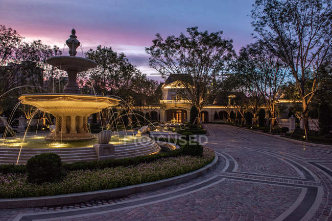 Belle fontaine illuminée arbres verts et bâtiments chinois dans la soirée — Photo de stock