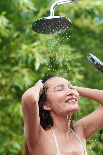 Beautiful happy young asian woman with closed eyes taking shower on green natural background — Stock Photo
