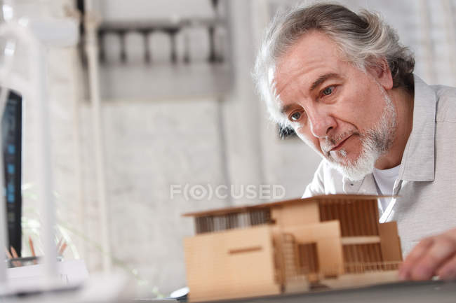 Профессионально сфокусированный зрелый архитектор, работающий с моделью здания на рабочем месте — стоковое фото