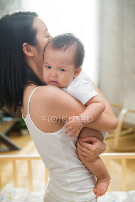 Seitenansicht einer jungen Mutter, die ihr unglückliches Baby zu Hause trägt — Stockfoto