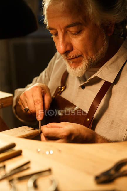 Vista de cerca del diseñador de joyas concentradas graves en delantal trabajando con anillo en el taller - foto de stock