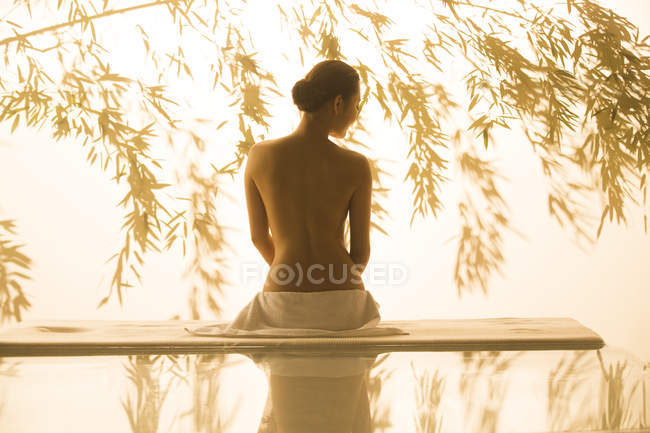 Вид ззаду гола молода жінка сидить на масажному столі в спа-салоні, тоноване зображення — стокове фото