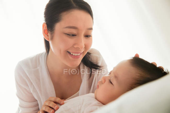 Happy young asian woman looking at her lovely baby sleeping on bed — Stock Photo