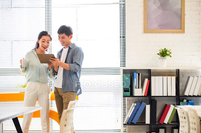 Sorridente jovem empresário e empresária usando tablet digital juntos no escritório moderno — Fotografia de Stock