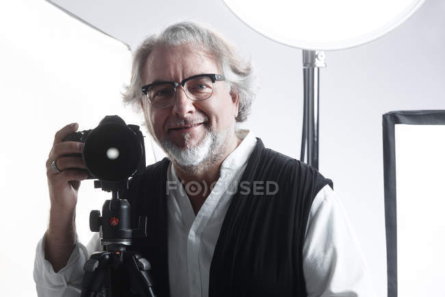 Photographe mature professionnel travaillant avec un appareil photo et souriant au studio de caméra — Photo de stock