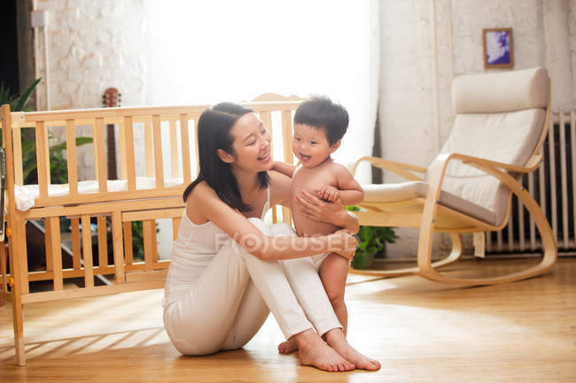 Full length vista de feliz jovem mãe abraçando adorável criança de pé no chão em casa — Fotografia de Stock