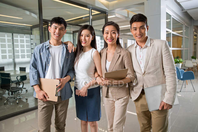 Professional young business team holding clipboards and digital devices, standing together and smiling at camera in office — Stock Photo