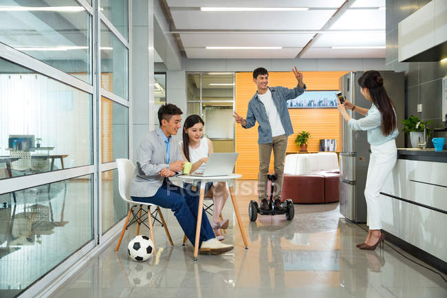 Happy young asian business colleagues having fun with soccer ball and self-balancing scooter during break in office — Stock Photo