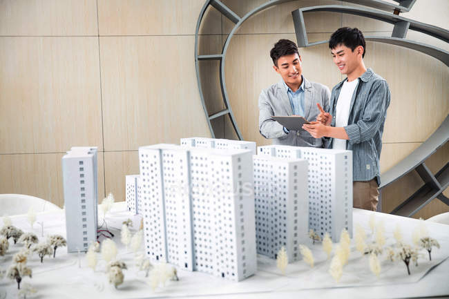 Lächelnde junge männliche Architekten mit digitalem Tablet und diskutieren Projekt im Büro — Stockfoto