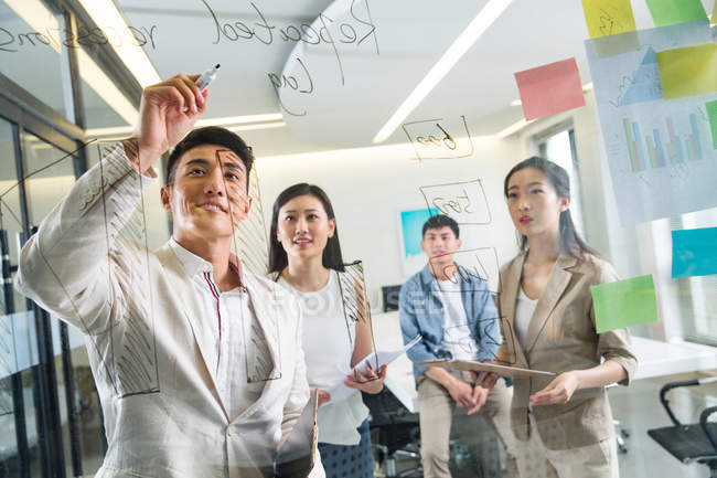 Vue à travers le verre de jeunes gens d'affaires asiatiques prendre des notes lors de la réunion au bureau — Photo de stock