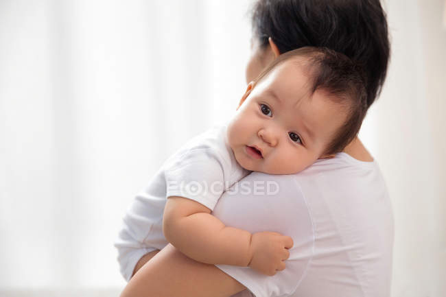 Vista lateral de la madre joven llevando bebé adorable en casa - foto de stock