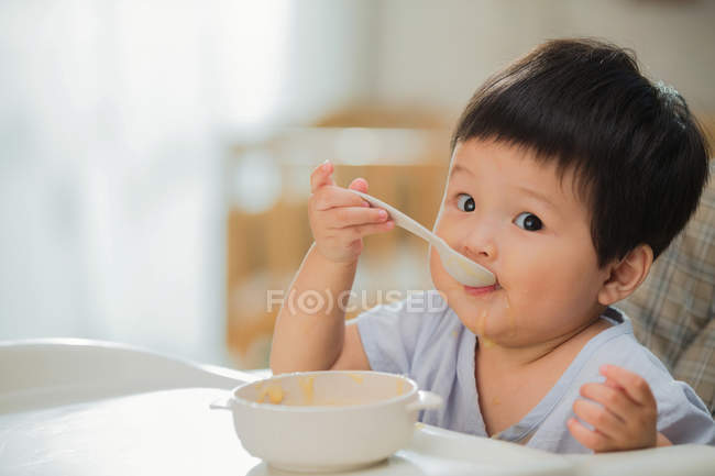 Чарівна азіатська дитина малюка тримає ложку і їсть вдома — стокове фото