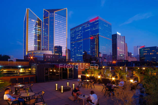 Personas sentadas en sillas en la terraza y hermosa vista nocturna de la ciudad de Beijing - foto de stock