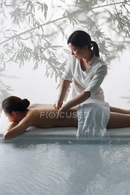 Vista ad alto angolo di massaggiatore femminile che fa massaggio corpo a giovane donna in spa — Foto stock
