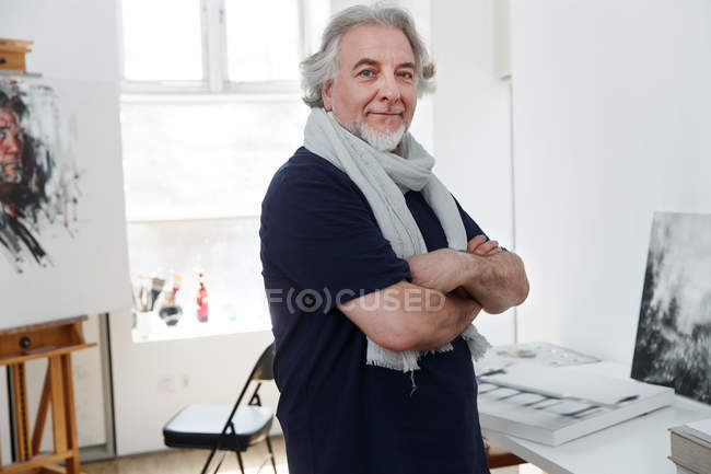 Bonito maduro masculino artista de pé com cruzados braços e sorrindo para câmera no estúdio — Fotografia de Stock