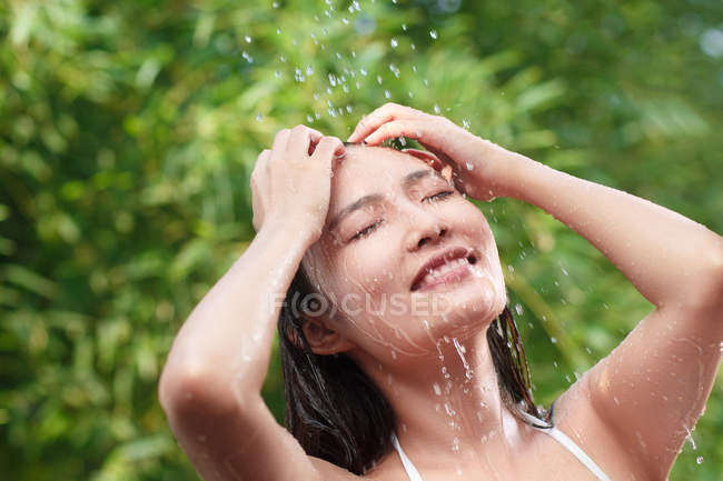 Beautiful happy young asian woman with closed eyes taking shower on green natural background — Stock Photo