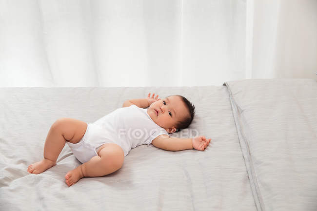 Младенец, лежащий на кровати и смотрящий в камеру, в полный рост — стоковое фото
