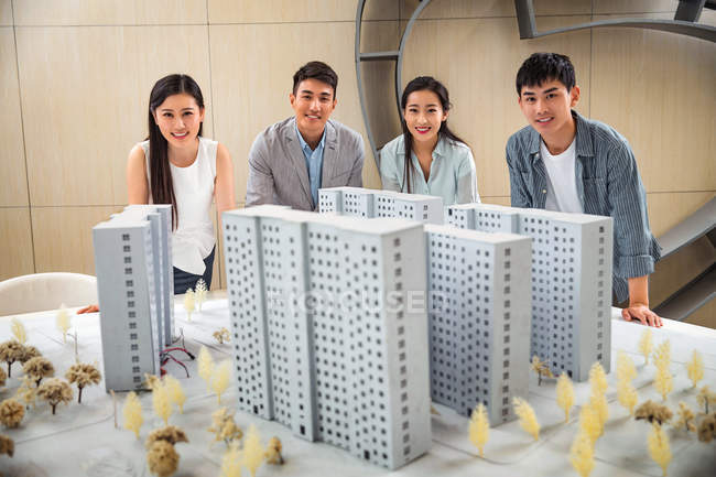 Profissional jovem asiático arquitetos de pé perto do projeto e sorrindo para a câmera no escritório — Fotografia de Stock