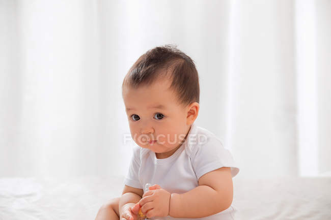 Чарівна азіатська дитина сидить на ліжку і тримає дитячу пляшку — стокове фото