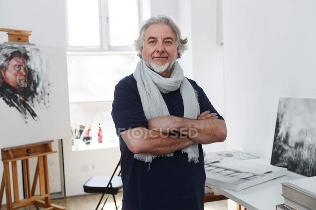 Bonito maduro masculino artista de pé com cruzados braços e sorrindo para câmera no estúdio — Fotografia de Stock