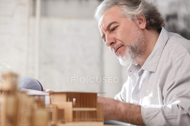 Arquitecto maduro enfocado profesional que trabaja con el modelo del plano y de la construcción en el lugar de trabajo - foto de stock