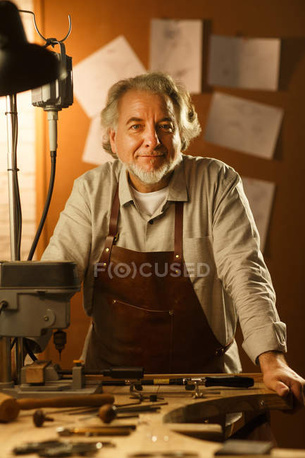 Professional jewelry designer in apron standing in workshop and smiling at camera — Stock Photo