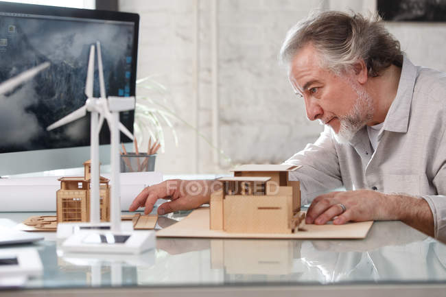 Vista laterale del professionista architetto maturo che lavora con il modello di costruzione sul posto di lavoro — Foto stock