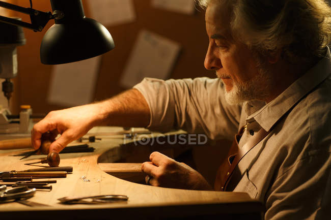 Vista lateral do designer de jóias profissional no avental sentado no local de trabalho — Fotografia de Stock