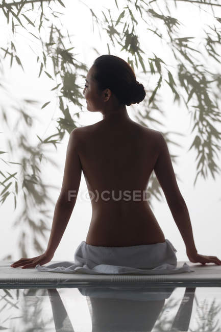 Rückseite der attraktiven jungen nackten Frau sitzt auf Massagetisch im Wellnessbereich — Stockfoto