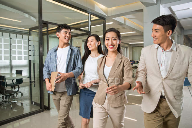 Щасливі молоді професійні азіатські бізнесмени і бізнес-леді ходять і спілкуються разом в сучасному офісі — стокове фото