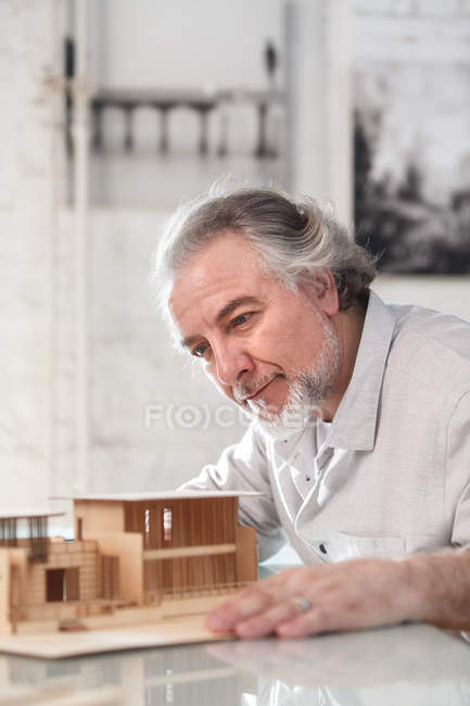 Професійний усміхнений зрілий архітектор працює з будівельною моделлю на робочому місці — стокове фото
