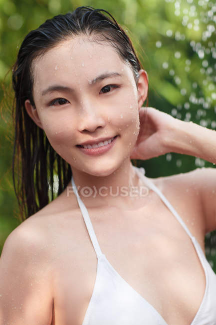 Hermosa joven asiática mujer en bikini tomando ducha y sonriendo a la cámara - foto de stock