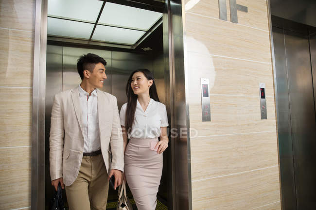 Happy young asian businessman and businesswoman smiling each other while walking from elevator in office — Stock Photo