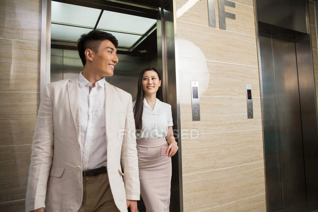 Smiling young asian businessman and businesswoman walking from open elevator — Stock Photo