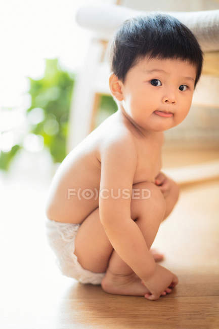 Vue pleine longueur de bébé asiatique adorable en couche accroupie et regardant la caméra à la maison — Photo de stock