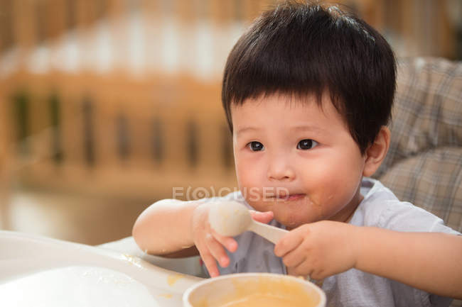 Крупним планом красивий азіатський малюк тримає ложку і їсть вдома — стокове фото